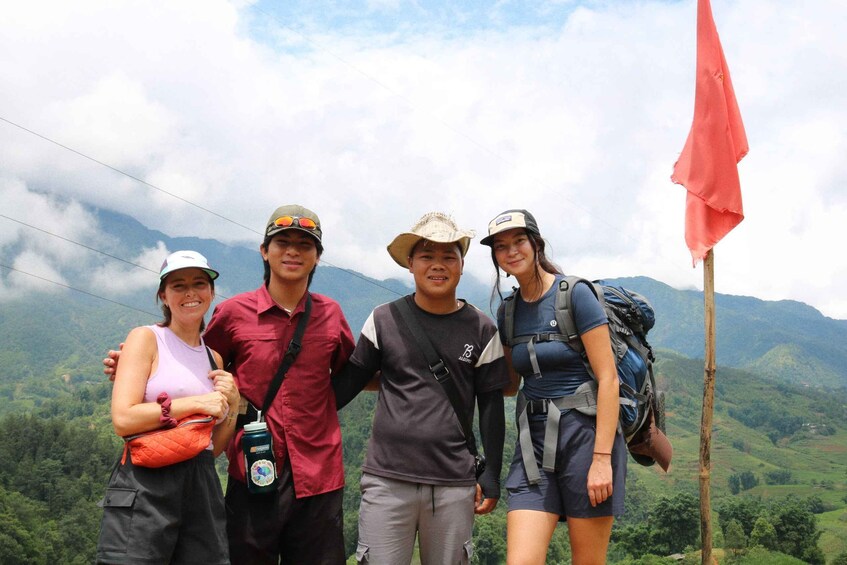 A group of people standing on a mountain with a red flag, surrounded by lush greenery and mountains in the background. 2