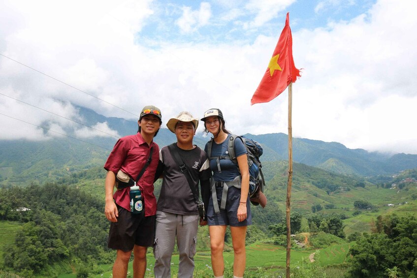 Three people standing in a mountainous landscape with a flag in the background. 5