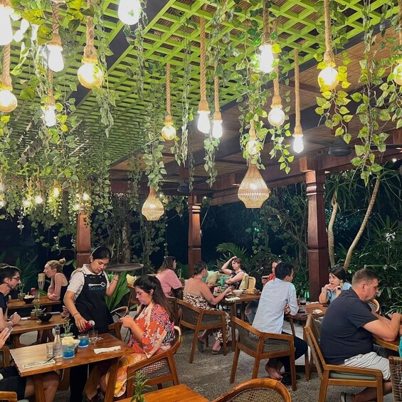 An outdoor restaurant with hanging light bulbs and greenery. 3