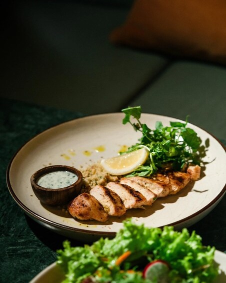 A plate with grilled chicken, a lemon wedge, and a small bowl of sauce. 2