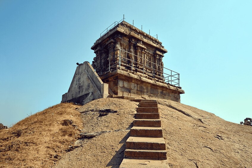 A stone structure with a staircase leading up to it, surrounded by dry grass and a clear sky. 4