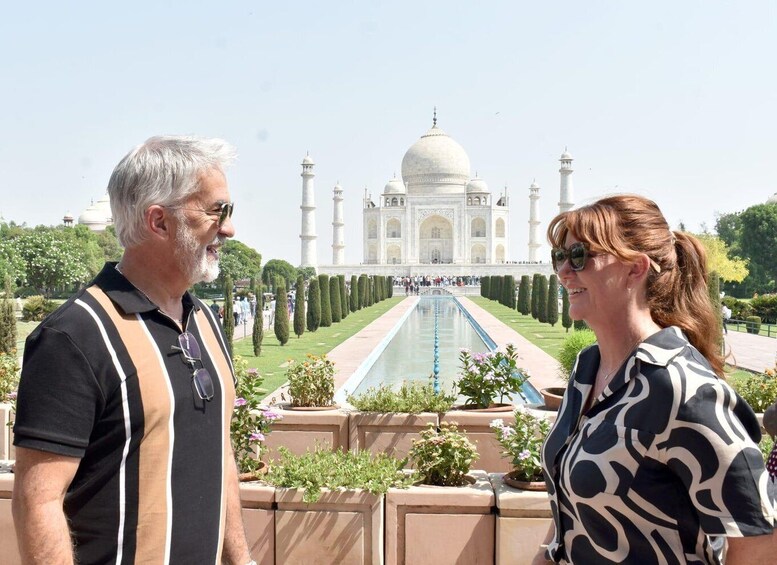 Two people standing in front of the Taj Mahal with a garden and a pool in the foreground. 4