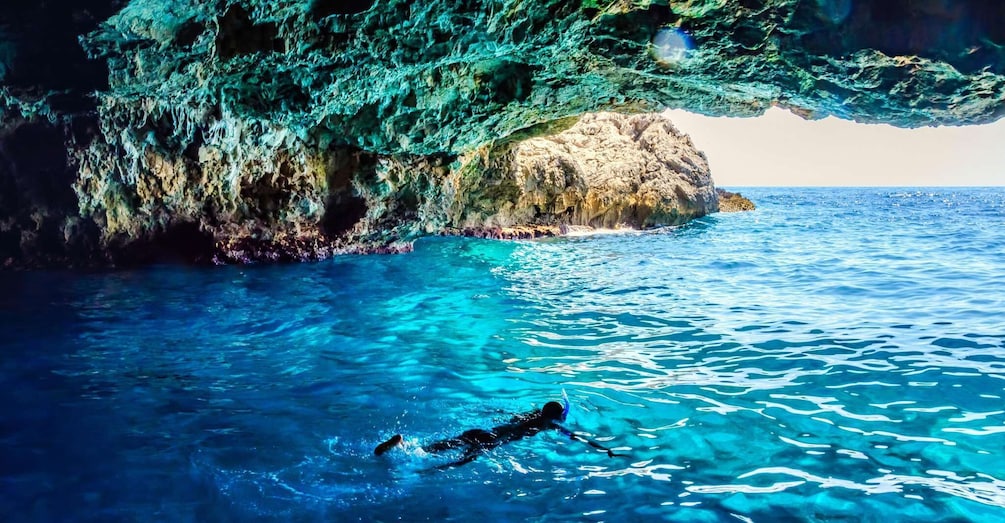 A swimmer in clear blue water near a rocky cliff. 1
