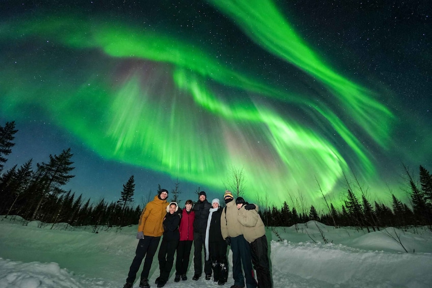 Un groupe de personnes se tient dans un paysage enneigé, sous un ciel nocturne illuminé par des aurores boréales. 5