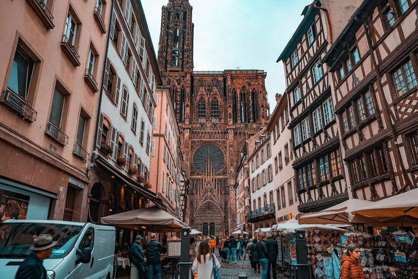 A bustling street with historic buildings, a prominent cathedral, and outdoor markets. 1