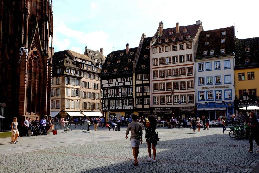 A cobblestone square with historic half-timbered buildings, a cathedral, and people walking. 3