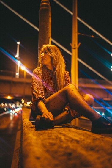A person sitting on a concrete ledge at night with city lights in the background. 5