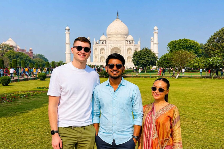 Three people standing in front of the Taj Mahal with a clear sky. 4