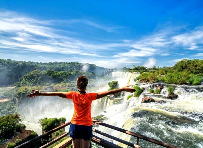 A person standing with arms outstretched overlooking a waterfall. 1