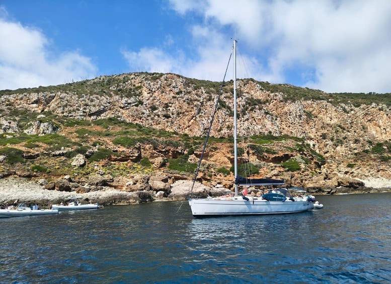 A sailboat anchored near rocky coastline with a clear sky. 4