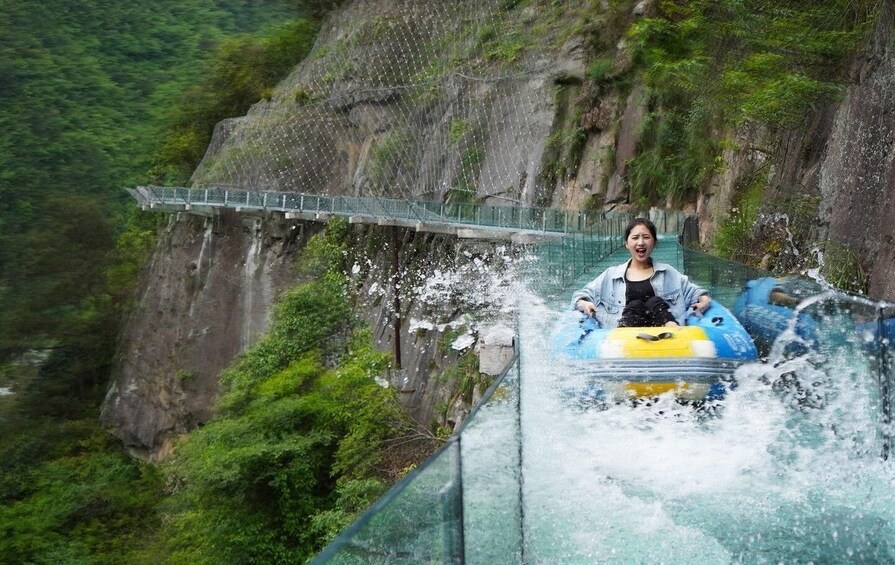 A person in a raft navigating a water slide with a glass bridge in the background. 2