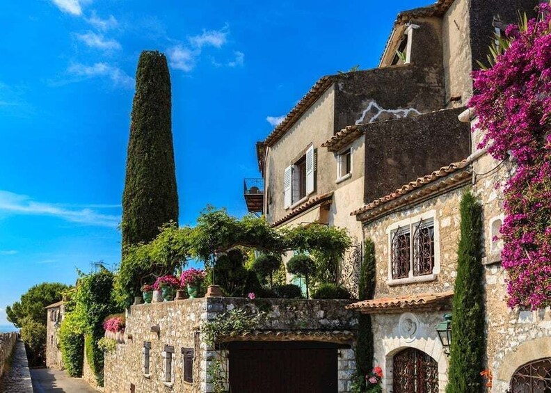 A narrow street lined with historic stone buildings, some with balconies and flowering plants. 5