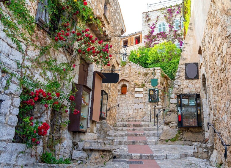 A narrow stone staircase leading up to a building with red flowers and greenery. 1