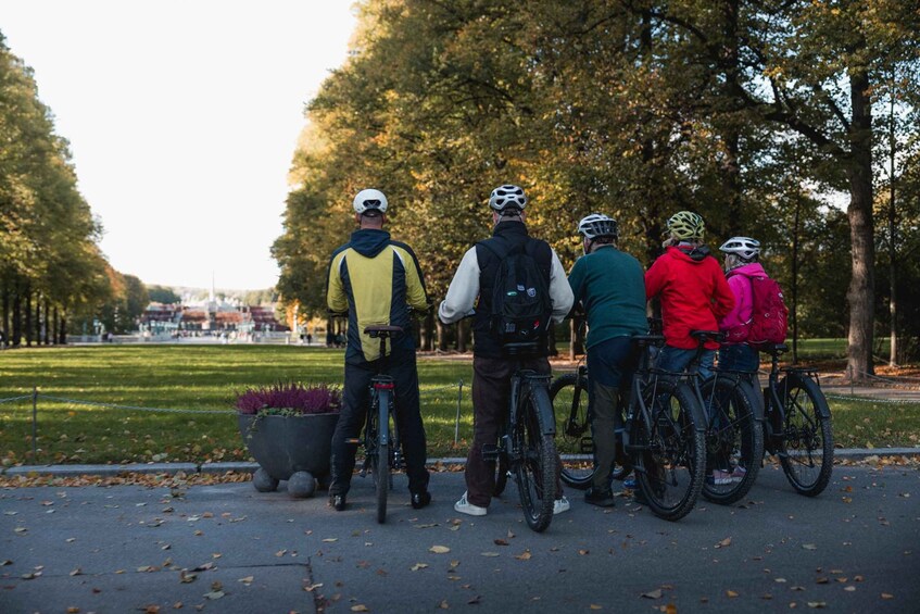 A group of cyclists in a park with trees and a paved path. 2