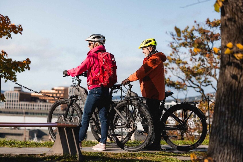 Two people with bicycles in a park with trees and a distant cityscape. 4