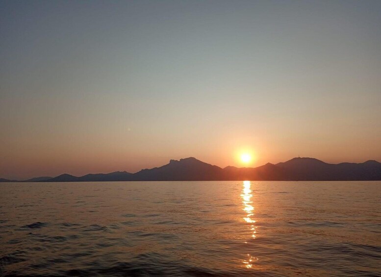 A sunset over a calm body of water with mountains in the background. 1