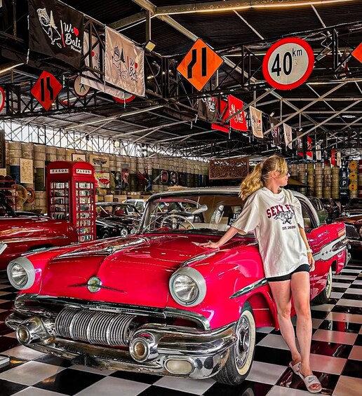 A vintage red car in a showroom with a woman standing beside it. 3