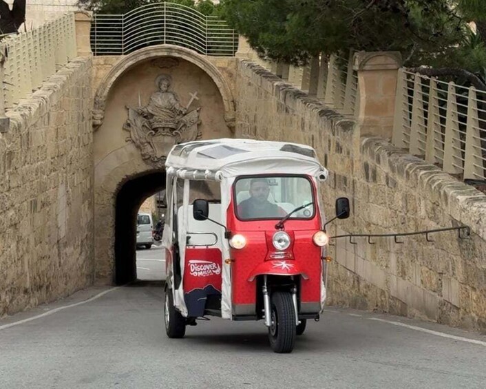 A red and white tuk-tuk driving through a stone tunnel. 1
