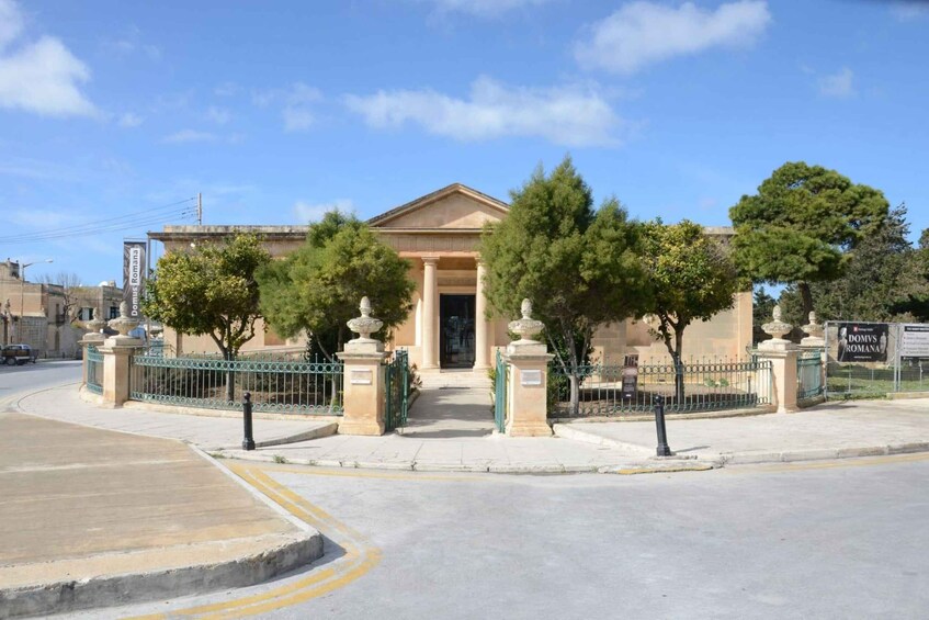 A classical building with columns, a gated entrance, and trees in front. 3