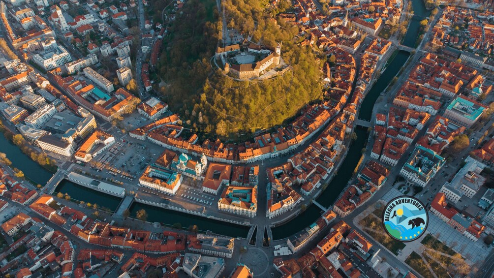 An aerial view of a historic city with a prominent castle surrounded by a fortified wall, a river, and a mix of traditional and modern architecture. 2