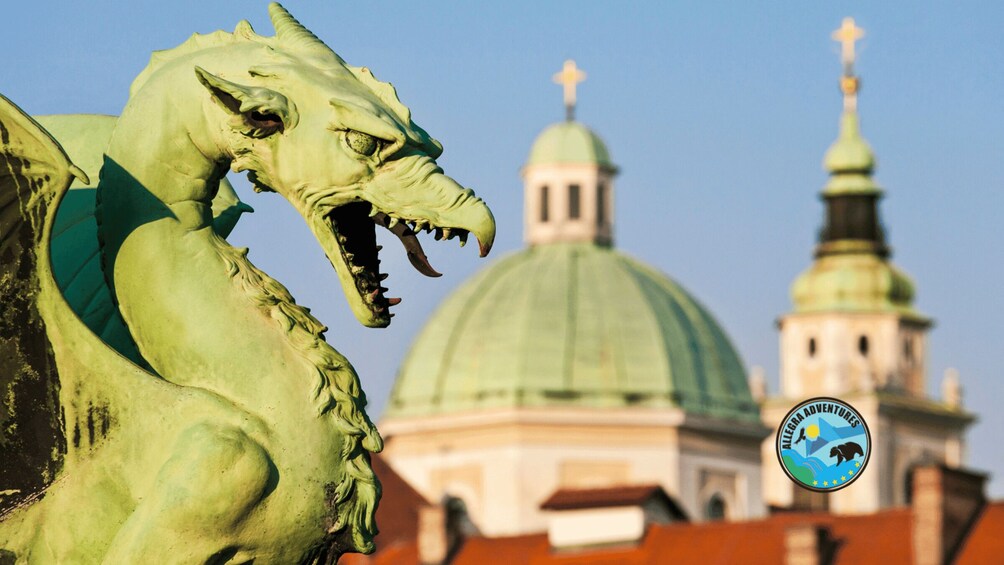 A green dragon statue in front of a building with a green dome and a tower with a cross on top. 3