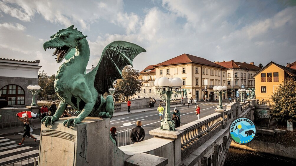 A dragon statue on a bridge with pedestrians and historic buildings in the background. 5