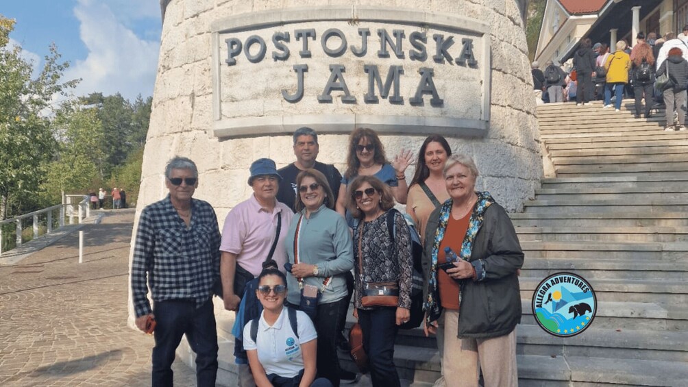 A group of people standing in front of a stone monument with the inscription "POSTOJSKA JAMA". 5