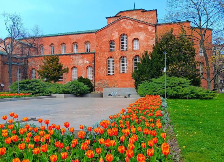 A red brick building with arched windows and a garden of orange tulips. 4