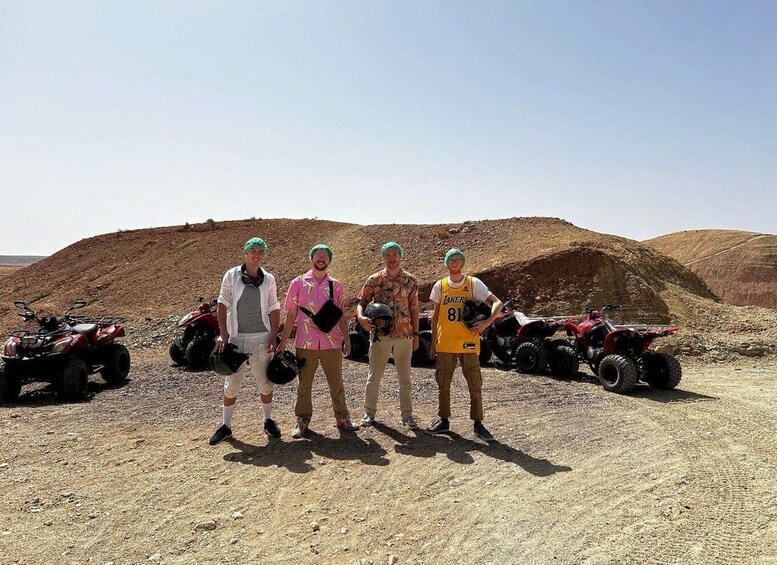 Four people standing in a desert with ATVs in the background. 3