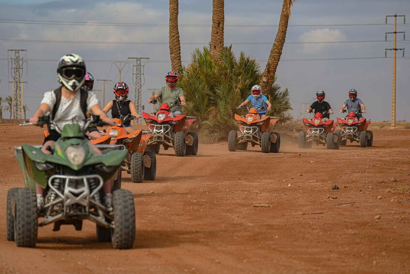 A group of people riding ATVs on a dirt road with palm trees and power lines in the background. 2
