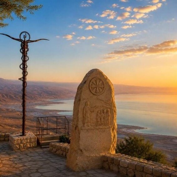 A stone monument with carvings, a metal sculpture, and a view of a valley with a body of water. 2