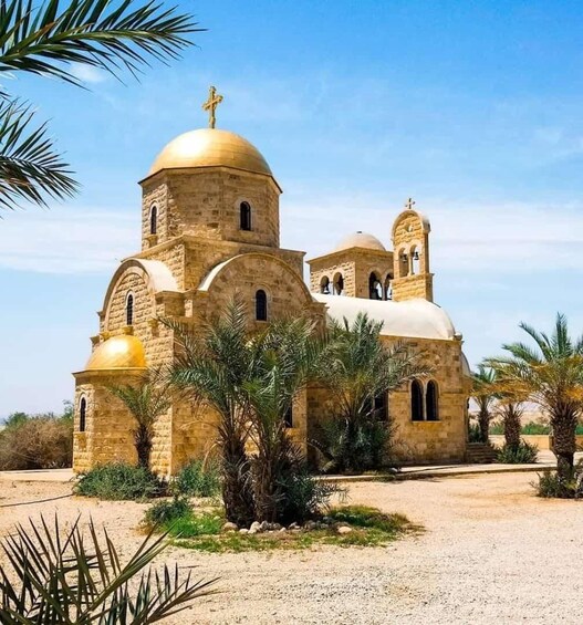 A church with a golden dome and cross, surrounded by palm trees and dry vegetation. 1