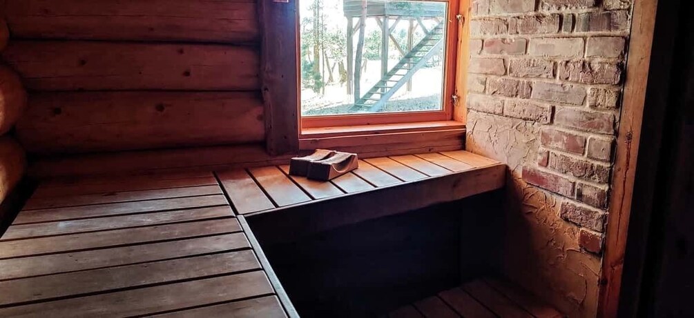 A wooden cabin interior with a bench, a window, and a brick wall. 3