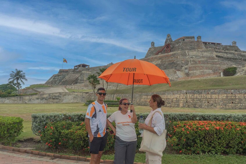 Three people standing in front of a historical fort with an orange umbrella. 1