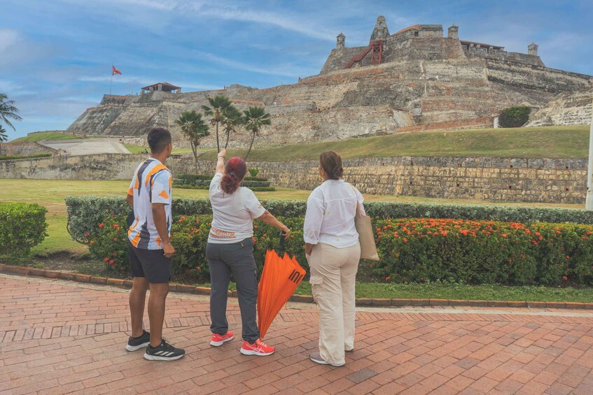 A historic fort with a flag, a paved walkway, and a garden with red flowers. 2