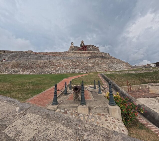 A historical fort with a red pathway leading to a large cannon, surrounded by stone walls and greenery. 4