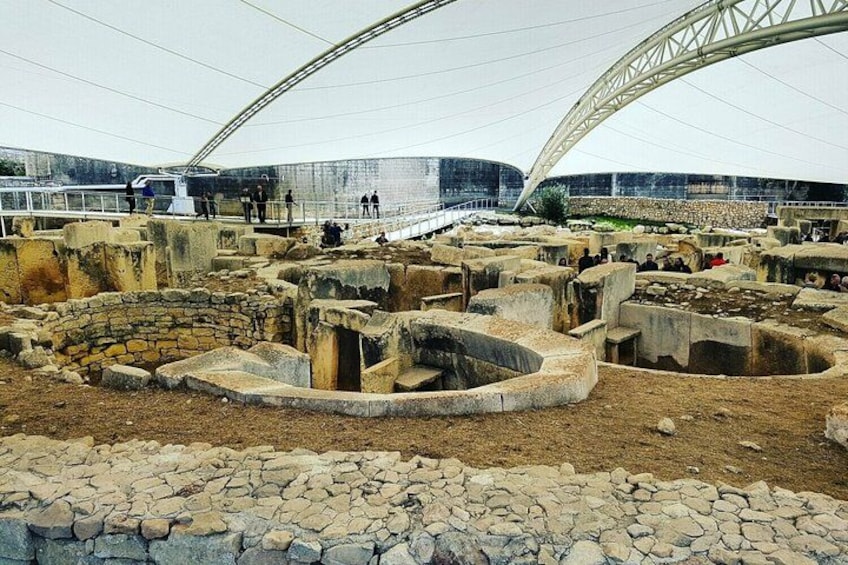 An archaeological site with ancient ruins and a large, modern structure in the background. 1
