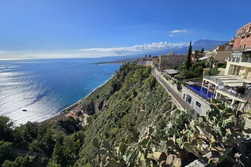 A coastal town with a cliffside road, buildings, and a view of the sea and distant mountains. 3