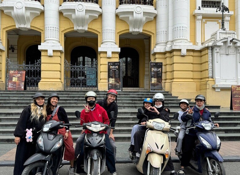 A group of people on scooters in front of a yellow building with white columns and balconies. 3