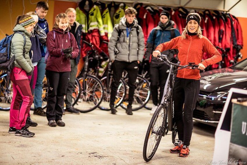 A person on a bicycle in a store with bicycles and winter clothing in the background. 2