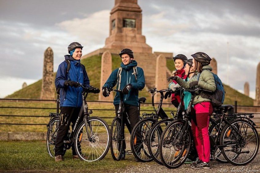 A group of cyclists standing with bicycles in front of a historical monument. 3