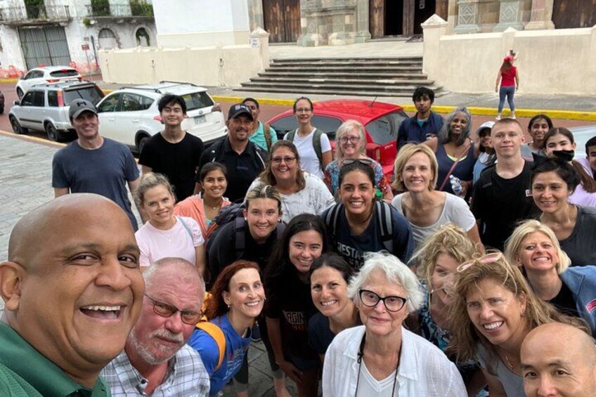 A group of people posing for a photo in front of a building with steps and a red car parked nearby. 4