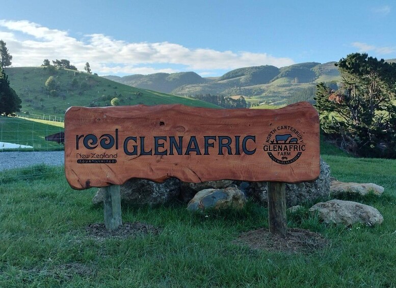 A wooden sign with 'reol glenafric' and 'North Canterbury Glenafric Farm' text, set against a rural landscape with hills and trees. 5