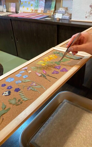 A person painting a corkboard with floral designs. 1