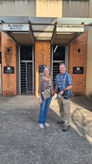 Two people standing in front of a building with signs reading 'BLANKES WHITES' and 'NIE - BLANKES NON -WHITES'. 3