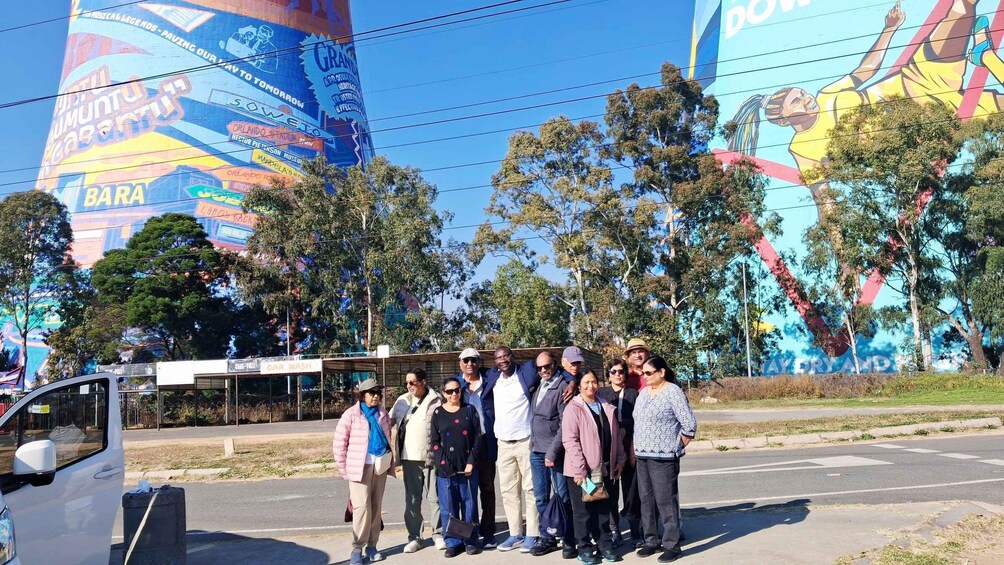 A group of people standing in front of a large mural with text and images, including 'ORLANDO STADIUM' and 'HECTOR PETERSON MUSEUM'. 4