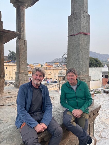 Two men sitting on stone structures with a cityscape in the background. 2