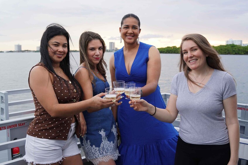 Four people toasting with drinks on a boat with a city skyline in the background. 4