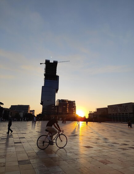A person riding a bicycle in an open plaza with a sunset in the background. 3