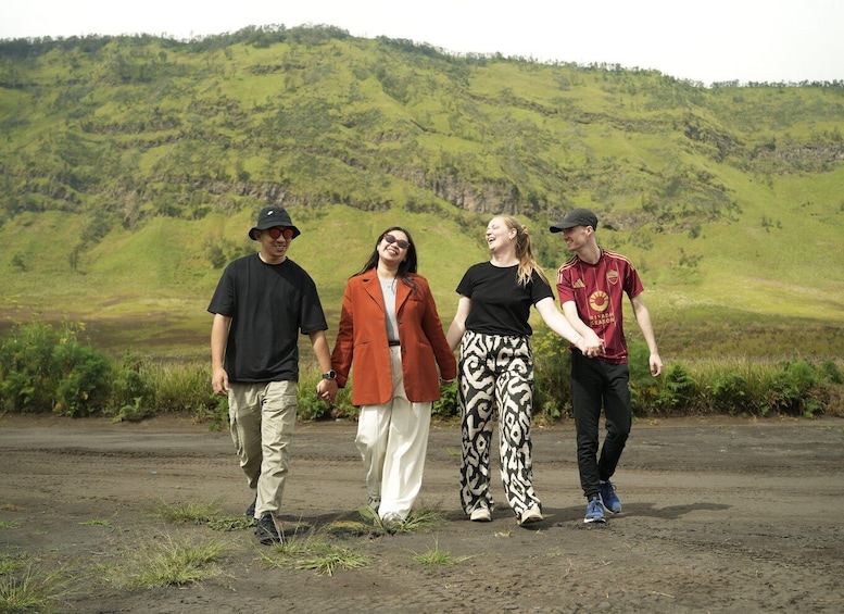 Four people walking on a dirt path with a green hillside in the background. 3